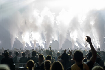 Crowd of people attending a musical performance. Bright light coming from the stage with smoke effects