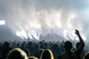 Crowd of people attending a concert. Bright light coming from the stage with smoke effects