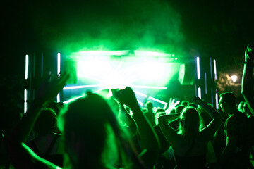 Crowd of people attending a musical performance with hands up. Bright light rays coming from the stage