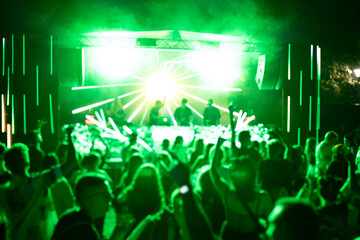 Crowd of people attending a musical performance with hands up in the air. Bright neon green light...