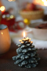 Cup of tea or coffee, glass of wine or juice, bowl of cookies, organic pomegranate, fluffy blanket, pine cones, various Christmas decorations and lit candles on the table. Christmas hygge concept.