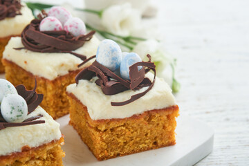 Easter carrot cake bars decorated with chocolate nest and chocolate candy eggs blossoming cherry or apple flowers on rustic light wooden backgrounds. Easter holiday meal. Traditional Easter food.