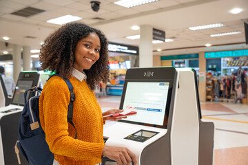 Black women with short, curly hair check-in via automatic machines by themselves in the airport to...