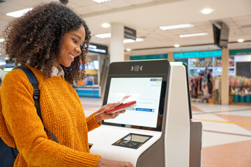 Black women with short, curly hair check-in via automatic machines by themselves in the airport to travel or study abroad. - obrazy, fototapety, plakaty