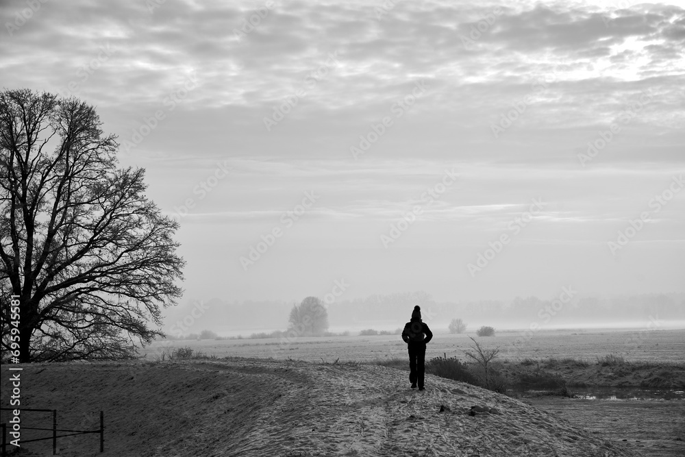 Wall mural woman walking in the snow on the warta river during winter