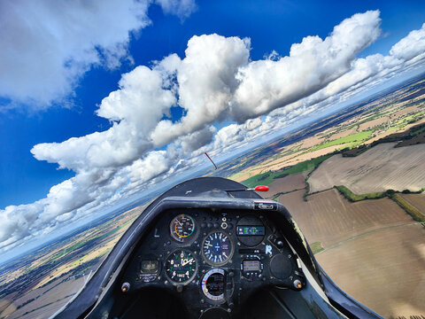 Glider plane cockpit in flight. Blue sky, clouds and fields seen from a sailplane