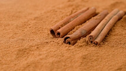Aromatic spices creative concept advertisement. Close-up studio shot of spices. Brown aromatic cinnamon sticks lying on ground cinnamon powder. A shot for a coffee shop or restaurant.