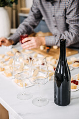 Wine Tasting Preparation with Cheese Pairings. Sommelier prepares for a wine tasting event, carefully pairing various cheeses with wines, featuring an unopened bottle and elegant glasses.