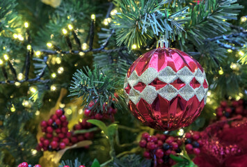 Red faceted Christmas ball with gold sparkles on Christmas tree with berries and a garland.