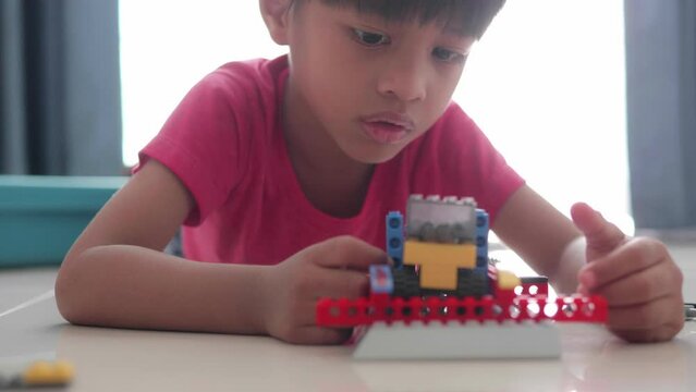 Adorable Asian boy, about 3-6 years old playing with miniature blocks as a toy windmill and having various toy accessories happily placed on the table inside his home, white background.	