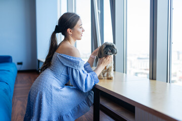 Female rests near windowsill with picturesque view in background. Woman sits with shih tzu in...