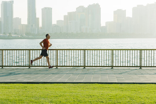 Senior man running by empty seafront promenade in sunshine morning. Healthy lifestyle in city.