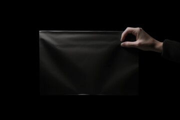elegant and mysterious image showing a hand delicately holding the corner of a glossy, black, opaque bag on an all consuming black background