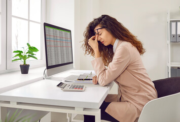 Stressed, tired young woman financial accountant with eye strain and headache holding her nose bridge while sitting at working desk with computer in office. Pain, stress at work, overworking concepts