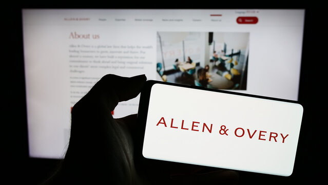 Stuttgart, Germany - 12-17-2023: Person holding smartphone with logo of British law firm Allen and Overy LLP in front of website. Focus on phone display.