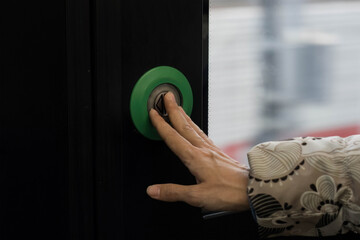 Female hand presses the door control green button to open doors in transport.