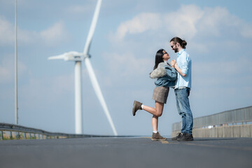 On the road, a young couple proposes to each other, with wind turbines in the background.