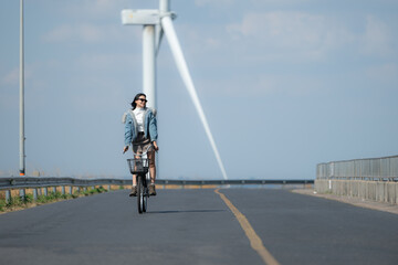 Young woman riding a bike on a road in a windmill.