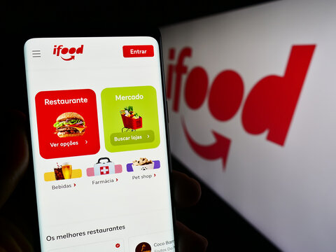 Stuttgart, Germany - 12-18-2023: Person holding cellphone with web page of Brazilian food ordering and delivery company iFood in front of logo. Focus on center of phone display.
