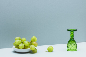 A dish with grapes and an empty inverted green wine glass on a bluish background.