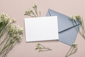 Gray envelope and empty card on a brownish background with a bouquet of small white flowers....