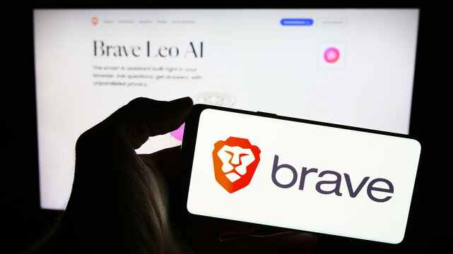 Stuttgart, Germany - 12-18-2023: Person holding mobile phone with logo of American web browser company Brave Software Inc. in front of business web page. Focus on phone display.