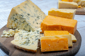 English cheeses collection, mature and coloured cheddar cheese and semi-soft, crumbly old stilton blue cheese close up