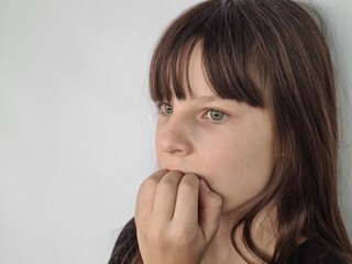Fototapeta premium Beautiful girl standing looks tense and nervous with her hands in mouth and biting nails