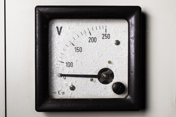 Old analog voltmeter with an arrow and cracked paint on a scale with numbers. Electrical measuring and control device