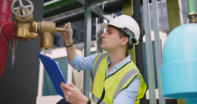 A engineer under checking inspects the industry factory pressure water pump valves equipment in a substation for the distribution of clean water at a large industrial. Water pipes. Industrial plumbing