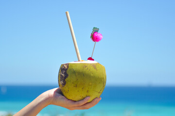 Colourful cocktail in fresh coconut with a straw and pink decoration held in hand. 
