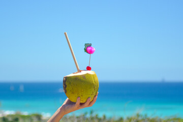 Colourful cocktail in fresh coconut with a straw and pink decoration held in hand. 