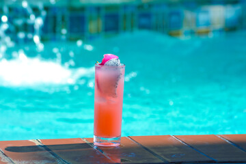 A glass of cold pink juice with passion fruit and ice on the pool side.