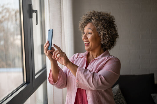 A cheerful mature woman is actively sending and receiving messages on her smartphone, spreading positive holiday vibes