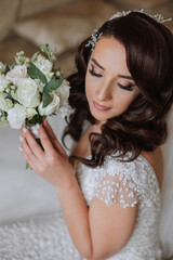 A wonderful beautiful portrait of a young bride. Beautiful bride with wedding makeup and jewelry wreath on long curly hair. Wedding photo model with brown eyes in a beautiful interior.