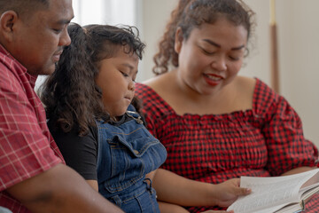 Obraz premium mother and girl are reading a book in living room. Asian chubby family relaxing with education program.