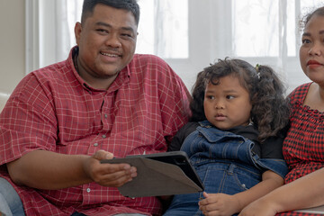 Happy Asian family using tablet. Asian Chubby father mother and kid playing game watching movies. Relaxing at home for lifestyle concept.