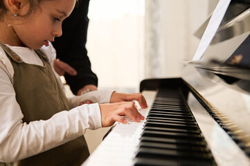 Child girl playing grand piano, touching piano keys, performing musical rhythm in individual music...