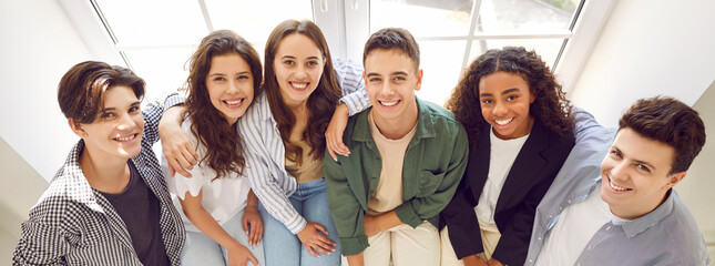 Cheerful diverse school friends having fun together. Banner with group portrait of happy multiethnic teenagers. Multiracial boys and girls sitting on window sill, looking at camera and smiling - obrazy, fototapety, plakaty