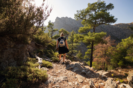 Back view of a backpacker girl hiking on a mountain trail in the lush Halari canyon on the mountainuous North Aegean Island of Ikaria.