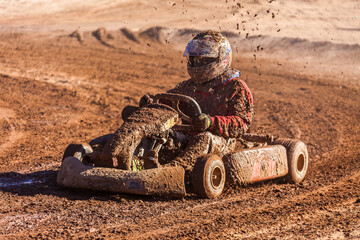Kart driver competing on a dirt track completely splashed with mud.