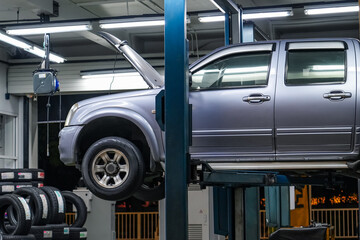 Pickup truck lifted into the air using a mechanical bridge jack in a service garage for car repair and maintenance at night time - obrazy, fototapety, plakaty
