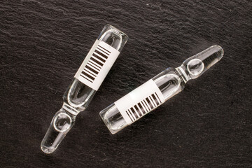 Two glass medical ampoules on slate stone, macro, top view.