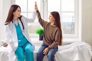 Portrait of a friendly paediatrician doctor giving high five with her little smiling girl patient sitting on the couch in medical clinic. Pediatric medicine and health care concept. - Powered by Adobe