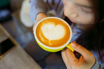 Closeup image of a cup of coffee with heart shape latte art, young woman drinking coffee in coffee...