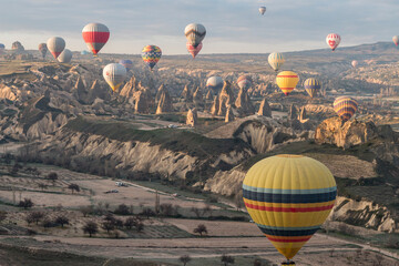 numerous hot air balloons flying over sun-lit fairy chimneys in Cappadocia, Göreme, Turkey
