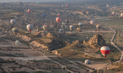 dozens of colorful hot air balloons flying over the landscape of Cappadocia in the early morning,...