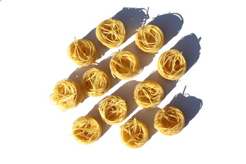 A lot of spaghetti in the form of a nest lies on a white background.	