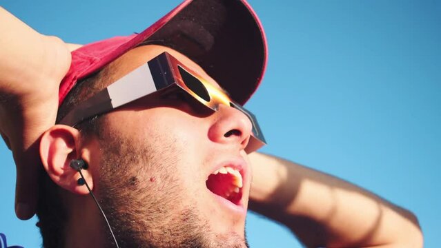 Portrait of man wearing cap and solar eclipse glasses, looking sun with blue sky at background 
