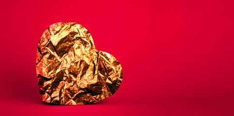 Golden foil heart on red background. Copy space.